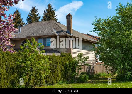 Außenansicht des Immobiliengebäudes mit wunderschönem Garten an einem sonnigen Tag. Großes maßgeschneidertes Haus mit Garten, Zaun und grünem Rasen in den Vororten in ca. Stockfoto