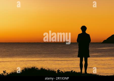 Silhouette eines Mannes, der bei Sonnenaufgang auf einer Sanddüne mit Blick auf Jimmy's Beach steht. Hawks Nest im Zentrum von NSW Australien Stockfoto