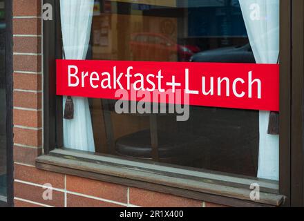 Ein Schild in einem Café-Fenster, auf dem ein komplettes Frühstück plus Mittagessen angezeigt wird. Mittagspause auf roter Anzeigetafel in einem Restaurant. Niemand, Platz für Text kopieren Stockfoto