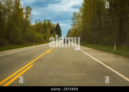 Rückansicht eines Autos, das im Sommer auf der Autobahn im Wald fährt. Trans-Canada Highway in British Columbia, wunderschöne Straße an einem bewölkten Frühlingstag. Stockfoto