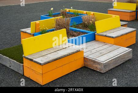 Farbenfrohe Holzbänke im Stadtpark. Gartenmöbel. Hölzerne Sitzbänke mit Blumenbeet. Niemand, Straßenfoto Stockfoto