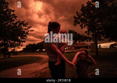 Sanger, Texas, USA. 15. Mai 2023. Der Himmel von Texas färbt sich in tiefem Orange, während sich eine große Sturmzelle durch den Nordosten bewegt, 5/15/23 Sanger, Texas. Es wurde von starkem Hagel und starkem Wind berichtet. Courtney Olson (links), schaut mit ihren Kindern nach draußen, um den sich ändernden farbigen Himmel zu sehen, der apokalyptisch aussieht. (Kreditbild: © Chris Rusanowsky/ZUMA Press Wire) NUR REDAKTIONELLE VERWENDUNG! Nicht für den kommerziellen GEBRAUCH! Kredit: ZUMA Press, Inc./Alamy Live News Stockfoto