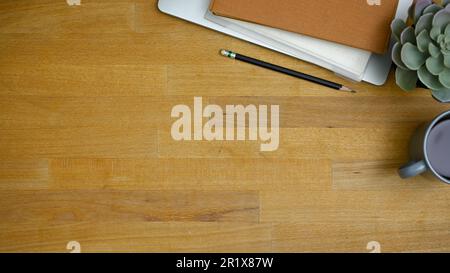 Arbeitsbereich von oben, flach liegend mit Bleistift, Büchern, saftiger Pflanze, Kaffeetasse und Kopierbereich auf Holzhintergrund. Stockfoto