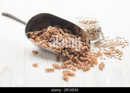 Grüne Linsenfusilli-Pasta auf Holzhintergrund. Eine Portion rohe Pasta und grüne Linsen. Glutenfreie Pasta. Stockfoto