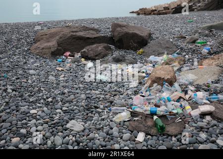 Müll verstreut auf Kieselsteinen nahe dem Meer. Recycling-Problem Stockfoto