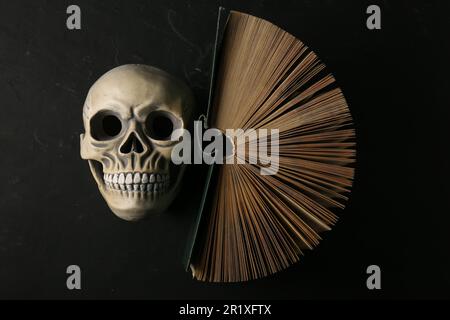 Menschlicher Schädel und altes Buch auf schwarzem Tisch, Draufsicht Stockfoto