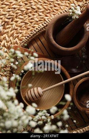 Holzschüsseln, Walznadel und Honigstiel in der Nähe von Blumen auf Korbmatte, flach liegend Stockfoto