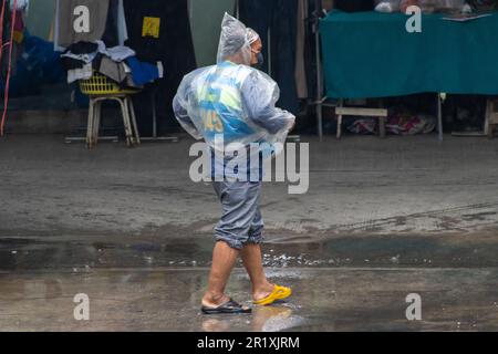 SAMUT PRAKAN, THAILAND, MAI 10 2023, Ein Taxifahrer auf einem Motorrad läuft mit einem Regenmantel und verschiedenen Schuhen eine regnerische Straße entlang Stockfoto