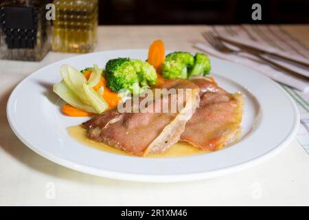 Schweinelende mit Speck bedeckt und serviert mit Gemüse wie Brokkoli oder Karotten. Stockfoto