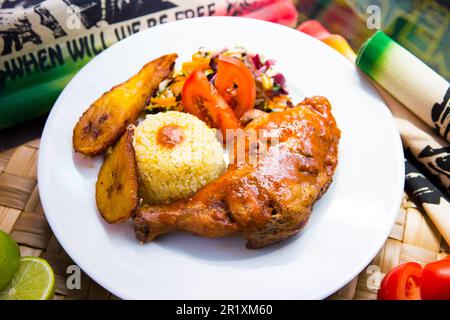 Gebackenes Hähnchen auf Schenkelbasis, serviert im jamaikanischen Stil mit Reis, Salat und Banane. Stockfoto