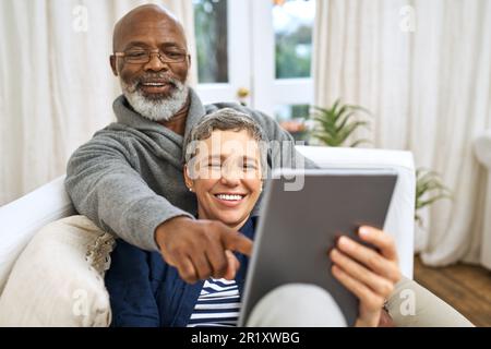 Technologie, Seniorenpaar mit Tablet und Sofa, glücklich im Wohnzimmer ihres Zuhauses. Soziale Medien oder Streaming, Ruhestand oder Entspannung und glückliche Ehe Stockfoto
