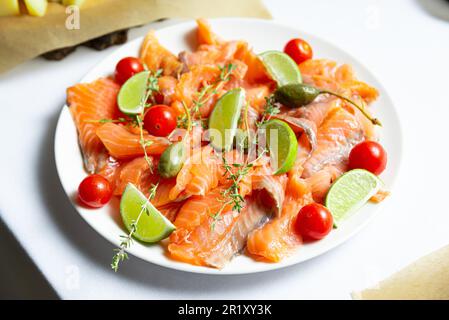 Lachs-Carpaccio mit Tomaten, Oliven und Limette auf weißem Teller Stockfoto