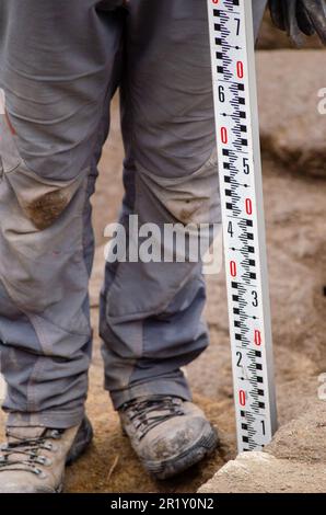 Arbeiter, die eine Teleskopnivellierplatte halten, hilft Vermesser, Geodesiker, Position und Tiefe auf der Baustelle zu messen. Stockfoto