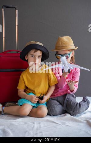 Fröhliche Kinder in Sommerkleidung spielen mit dem Flugzeug. Das Konzept des Sommerurlaubs mit der Familie. Studiofoto. Stockfoto