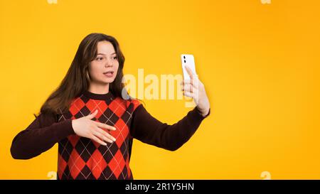 Junge Frau filmt sich am Telefon und Gesten auf gelbem Hintergrund Stockfoto