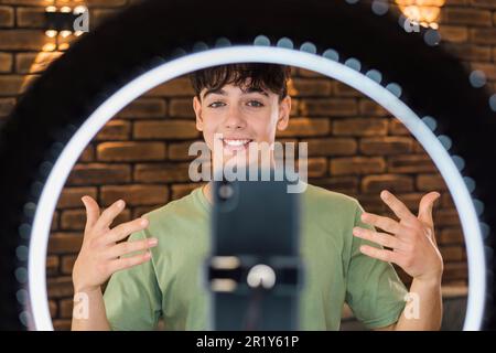 Ein junger lächelnder Mann Blogger Influencer, der sich selbst auf einem Smartphone auf einem Stabilisator in einer Küche erschoss Stockfoto