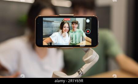 Junge lächelnde Blogger-Influencer, die sich mit einem Smartphone auf einem Stabilisator in einer Küche unterhalten und fotografieren Stockfoto