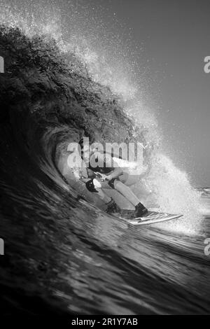 U-Bahn-Fahrt vom Wasser aus fotografiert. Die brechende Welle umrahmt die Surferin Carwyn Williams perfekt in Position mit einer Hand in Friedenszeichen Stockfoto