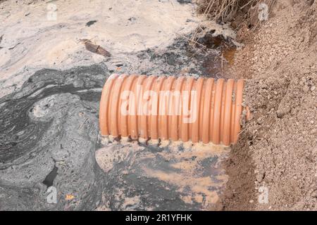 Abflussrohr mit fließendem Wasserstrom. Sturmwassermanagement in öffentlichen Räumen, Kunststoffrohren, Steinen und Sträuchern. Plastikrohre für die Naht Stockfoto