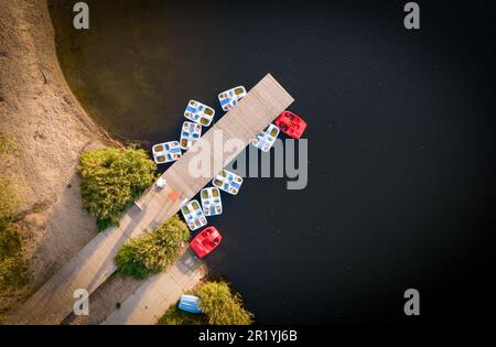 Tretboote (Tretboot, Wasserfahrrad, Tretboot) bleiben am hölzernen Pier (Yachthafen) auf dem See (Przylasek Rusiecki) mit der Drohne (Luftaufnahme von oben) Stockfoto