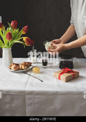 Frauenhände gießen Milch in den Kaffee. Das Frühstück steht auf dem Tisch. Stockfoto