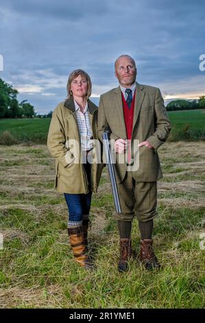 Eine englische Dame und ein Gentleman standen in der Dämmerung in Schießanzügen mit einer Schrotflinte Stockfoto