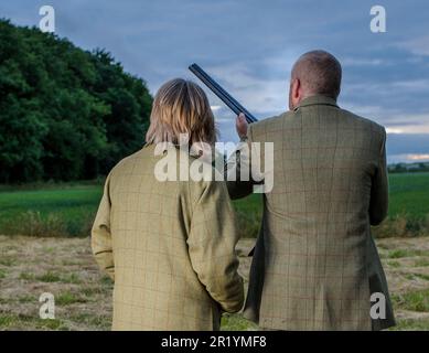 Eine englische Dame und ein Gentleman standen in der Dämmerung in Schießanzügen mit einer Schrotflinte Stockfoto