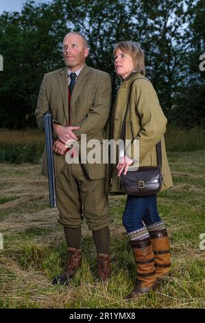 Eine englische Dame und ein Gentleman standen in der Dämmerung in Schießanzügen mit einer Schrotflinte Stockfoto