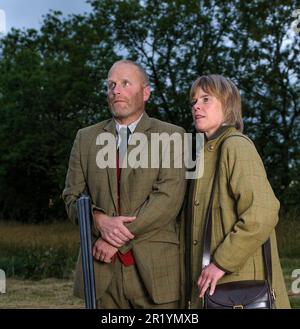 Eine englische Dame und ein Gentleman standen in der Dämmerung in Schießanzügen mit einer Schrotflinte Stockfoto