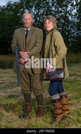 Eine englische Dame und ein Gentleman standen in der Dämmerung in Schießanzügen mit einer Schrotflinte Stockfoto