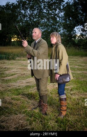 Eine englische Dame und ein Gentleman standen in der Dämmerung in Schießanzügen mit einer Schrotflinte Stockfoto