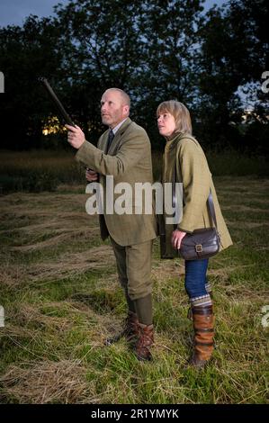 Eine englische Dame und ein Gentleman standen in der Dämmerung in Schießanzügen mit einer Schrotflinte Stockfoto