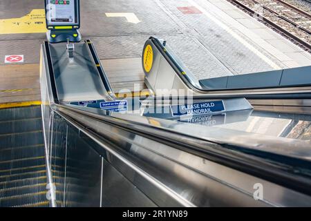 Eine Rolltreppe hinunter auf einen Bahnsteig am Bahnhof Reading. Schilder weisen darauf hin, dass Sie den Handlauf halten und sich rechts stellen müssen. Stockfoto