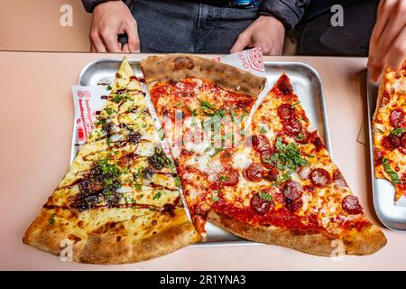 Ich schaue mir drei Scheiben Pizza an, die in einem Food Court in London, Großbritannien, zum Mittagessen gekauft wurden Stockfoto