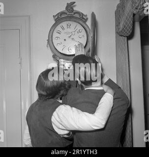 In den 1950er Jahren. Eine Frau und ein Mann vor einer antiken Uhr mit sichtbarem Uhrengesicht. Er passt die Zeit an, indem er die Schweden 1951 verschiebt. Conard Ref. 1870 Stockfoto