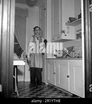 Mann der 1950er. Der schwedische Tänzer Mario Mengarelli in der Küche sieht so vorbereitet aus, wie man es von einem 1950er-Mann erwarten kann, trägt eine Schürze, hält eine Bratpfanne in der Hand und sieht verlegt aus. Schweden 1952 Ref. 1958 Stockfoto