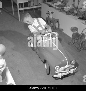 Junge in den 1950s. Auf der jährlichen Messe in Stockholm hat ein Stand mit Kinderspielzeug seine Ausstellung der neuesten verfügbaren Spielzeuge auf dem Markt. Der Junge probiert den Tretwagen aus und sieht glücklich aus. Schweden 1952 Conard Ref. 2112 Stockfoto