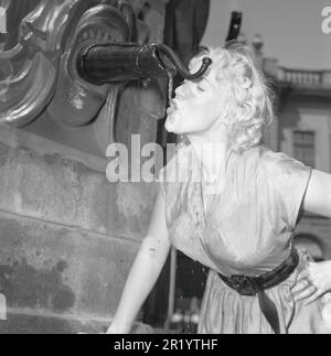 In den 1950er Jahren. Eine Frau trinkt das Wasser aus dem öffentlichen Brunnen Stortorgsbrunnen in Gamla Stan in Stockholm, Schweden. Der Brunnen wurde viele Jahre als Ort genutzt, von dem aus die Entfernungen von und zur schwedischen Hauptstadt gemessen wurden. 26. juni 1953 Stockfoto