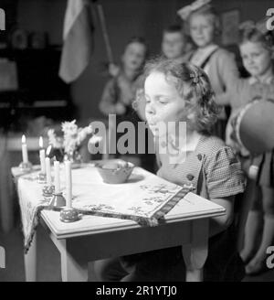 Geburtstag in den 1940er. Das Geburtstagskind sitzt an einem Schreibtisch, der mit brennenden Kerzen dekoriert ist. Eine Gruppe ihrer Freunde steht hinten und singt und spielt für sie. Sie wird gesehen, wie sie die fünf Kerzen ausbläst, damit sie heute fünf Jahre alt wird. Das Foto wird in einem Kindergarten in Stockholm mit Kindern im Alter von 4-6 Jahren aufgenommen. Schweden 1947. Conard Ref. 882 Stockfoto
