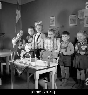 Geburtstag in den 1940er. Das Geburtstagskind sitzt an einem Schreibtisch mit fünf brennenden Kerzen. Es ist ihr fünfter Geburtstag. Eine Gruppe ihrer Freunde steht hinten und singt und spielt für sie. Das Foto wird in einem Kindergarten in Stockholm mit Kindern im Alter von 4-6 Jahren aufgenommen. Schweden 1947. Conard Ref. 882 Stockfoto