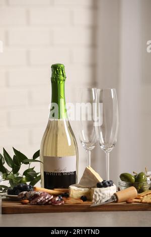Eine Flasche Weißwein, Gläser und köstliche Snacks auf einem grauen Tisch im Innenbereich Stockfoto