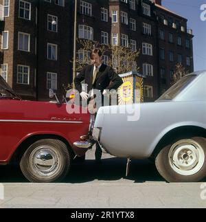 Fahren in der 1960er. Ein Mann steht bei zwei Autos, die entweder viel zu nah beieinander geparkt oder miteinander kollidiert sind. Der rote Opel Kadett steht so, dass die Stoßstange zum anderen Auto zeigt. Was der Mann mit seinem Gesichtsausdruck meint, ist schwer zu interpretieren, aber höchstwahrscheinlich besitzt er eines der Autos und ist natürlich nicht zufrieden mit dem, was er sieht. Schweden 1969 Kristoffersson Stockfoto