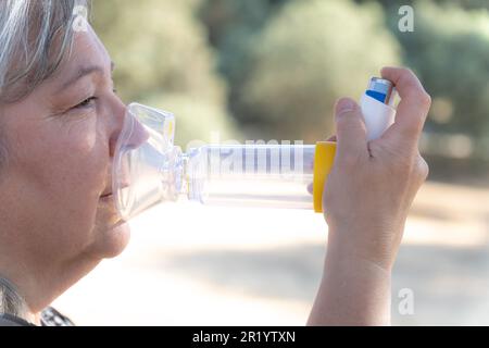 Frau verwendet einen Inhalator für Vernebler zur Behandlung von Atemwegserkrankungen. Sie ist auf dem Land, atmet frische Luft und genießt die Sonne. Stockfoto