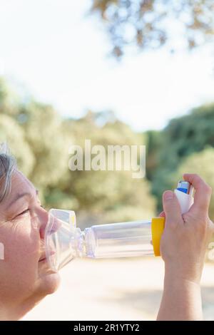 Frau verwendet einen Inhalator für Vernebler zur Behandlung von Atemwegserkrankungen. Sie ist auf dem Land, atmet frische Luft und genießt die Sonne. Stockfoto