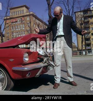 Fahren in der 1960er. Ein Mann steht vor seinem Auto, das bei einem Verkehrsunfall sichtbar beschädigt wurde. Ein Frontalaufprall oder jemand ist in sein Auto zurückgefahren. Er sieht frustriert aus. Schweden 1969 Kristoffersson Stockfoto