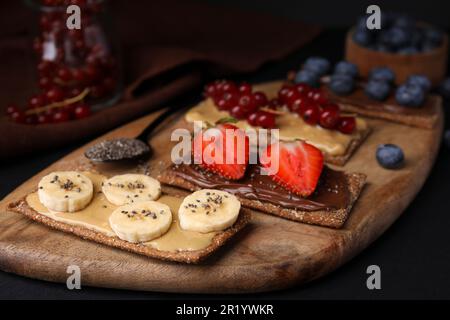 Frisches knuspriges Roggen-Knusperbrot mit verschiedenen Belägen auf schwarzem Tisch, Nahaufnahme Stockfoto