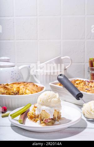 Süße Rhabarberbeerkuchen, selbstgemachter Schwammkuchen mit Rhabarber und Erdbeere, serviert mit Vanille-Eiskugel, auf sonnigen weißen Holzkrem Stockfoto