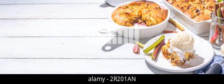 Süße Rhabarberbeerkuchen, selbstgemachter Schwammkuchen mit Rhabarber und Erdbeere, serviert mit Vanille-Eiskugel, auf sonnigen weißen Holzkrem Stockfoto