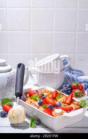 Süße Sommerbeerenkuchen, hausgemachter Schwammkuchen mit zuckerhaltigen Heidelbeeren und Erdbeeren, serviert mit Vanille-Eiskrem auf sonnigem, weißem Holz Stockfoto