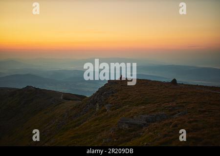 Ein Mann, der auf den Sonnenaufgang schaut. Berge bei Sonnenaufgang. Mann steht auf dem Gipfel. Natürliche Berglandschaft mit beleuchteten nebligen Gipfeln, nebligen Hängen und Tälern, Stockfoto